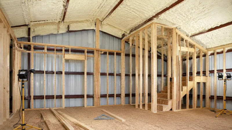 Wood-framed interior partition walls built inside a metal building shell, with spray foam across the metal roofline above