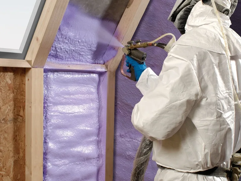 Installer spraying closed-cell foam in a sloped knee-wall ceiling beside a skylight